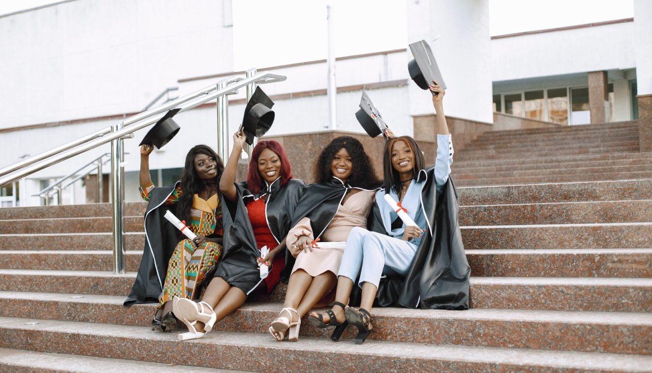 Graduate students sitting on stairs raising graduation caps